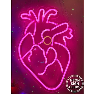 Peut inclure: Une enseigne au n&eacute;on rose vif en forme de c&oelig;ur humain. L'enseigne est bord&eacute;e d'une lumi&egrave;re rose vif et comporte un cercle jaune au centre. L'enseigne est suspendue &agrave; un mur et porte le texte "NEON SIGN CLUBS" dans un cercle blanc.