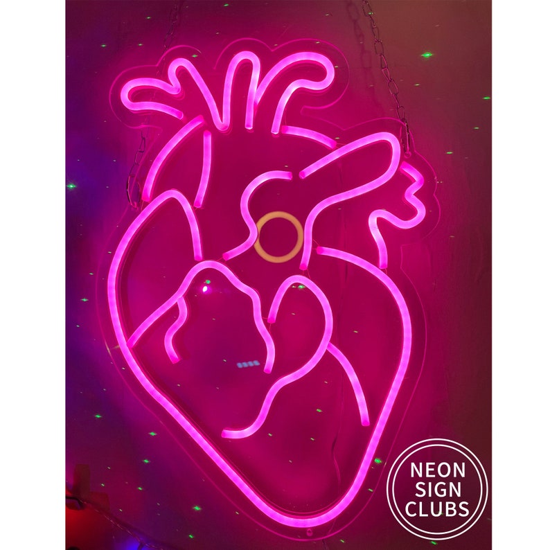 Peut inclure: Une enseigne au n&eacute;on rose vif en forme de c&oelig;ur humain. L'enseigne est bord&eacute;e d'une lumi&egrave;re rose vif et comporte un cercle jaune au centre. L'enseigne est suspendue &agrave; un mur et porte le texte "NEON SIGN CLUBS" dans un cercle blanc.