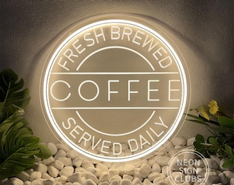 May include: A round, illuminated neon sign with the words "FRESH BREWED COFFEE SERVED DAILY" in white. The sign is surrounded by a white border and set against a neutral background with white stones and greenery. The sign also includes the text "NEON SIGN CLUBS".