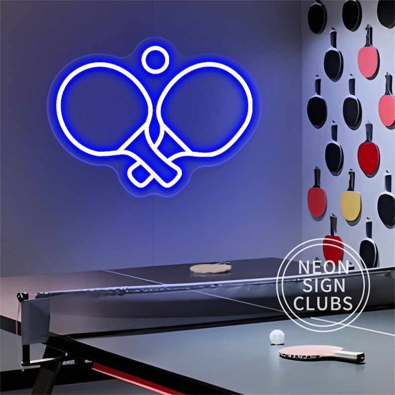 May include: A blue neon sign in the shape of two ping pong paddles and a ball. The sign is mounted on a blue wall above a ping pong table. The table has a net and a paddle and ball on it. The words "NEON SIGN CLUBS" are in a circle.