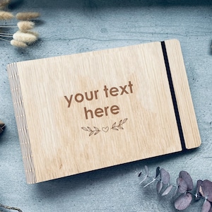 Könnte beinhalten: Ein Holzfotoalbum mit schwarzem Gummibandverschluss. Das Album hat eine natürliche Holzmaserung und der Text "your text here" ist auf der Vorderseite eingraviert.