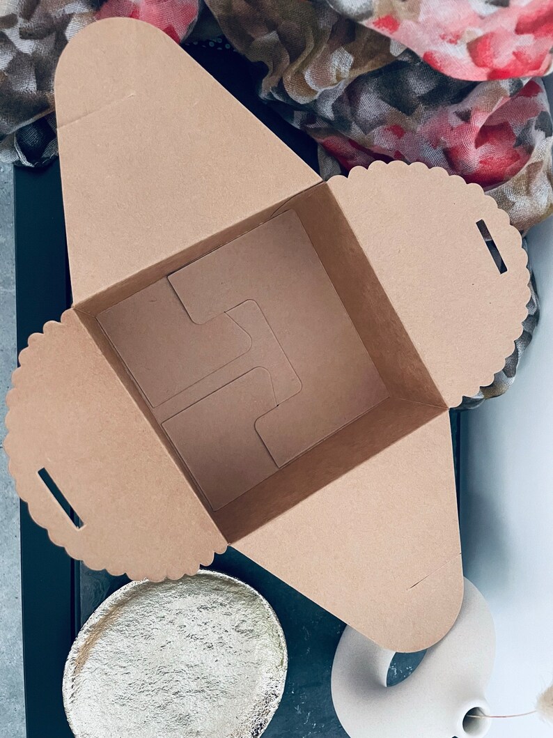 Puede incluir: Caja de cart&oacute;n marr&oacute;n cuadrada y abierta, con borde festoneado. Contiene un inserto interno para sujetar objetos. Sobre una superficie blanca, con un plato dorado y un jarr&oacute;n blanco.