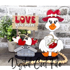 May include: A wooden Valentine's Day decoration featuring a goose wearing a red hat and holding a heart-shaped lock. A sign that says "LOVE you more" is also included, along with a picnic basket and hearts. The words "Digital Cut File" are written at the bottom.