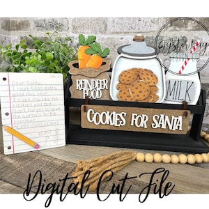 Puede incluir: Un letrero de Navidad de madera con el texto "Cookies for Santa" y una pequeña caja de madera con una jarra de leche, una bolsa de zanahorias y un tarro de galletas. El letrero está decorado con una pajita a rayas rojas y blancas. Una nota escrita a mano para Santa Claus está sobre la mesa junto al letrero.