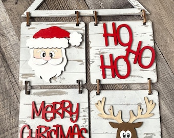 Puede incluir: Un letrero de Navidad de madera blanca con cuatro paneles. El panel superior tiene una cabeza de Papá Noel roja y blanca. El segundo panel dice "Ho Ho Ho" en letras rojas. El tercer panel dice "Feliz Navidad" en letras rojas. El cuarto panel tiene una cabeza de reno marrón con cuernos rojos y una nariz roja.