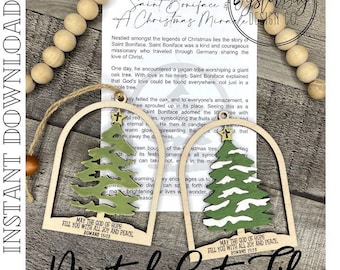 May include: Two wooden Christmas ornaments with a green and white Christmas tree design. The ornaments are shaped like a dome with a rounded top and a flat bottom. The ornaments have a white background with a green Christmas tree and white snow. The ornaments have the text "May the God of Hope fill you with all joy and peace. Romans 15:13" on the bottom.
