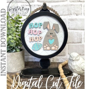 May include: A digital cut file for a DIY Easter craft project featuring a bunny, eggs, and the words "Hop Hop Hop". The design is perfect for creating a decorative sign or wall hanging.