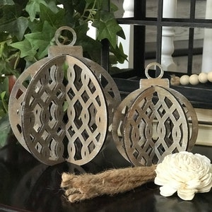 May include: Two wooden Christmas ornaments with a geometric design. The ornaments are a light brown color and have a distressed finish. They are sitting on a dark brown table with a white flower and a piece of twine.