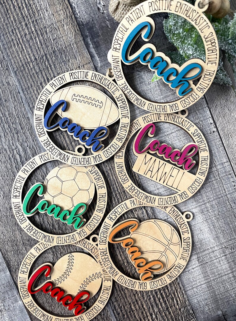 Peut inclure: Cinq ornements en bois avec le mot "Coach" &eacute;crit en diff&eacute;rentes couleurs sur chacun. Chaque ornement a un ballon de sport diff&eacute;rent au centre&nbsp;: un ballon de football am&eacute;ricain, un ballon de football, un ballon de basket-ball, un ballon de baseball et un ballon g&eacute;n&eacute;rique. Les mots "Respectueux, Patient, Positif, Enthousiaste, Soutenu, Confiant, Concentr&eacute;, Orient&eacute; vers les objectifs, Connaissant, Observable" sont &eacute;crits autour du bord de chaque ornement.