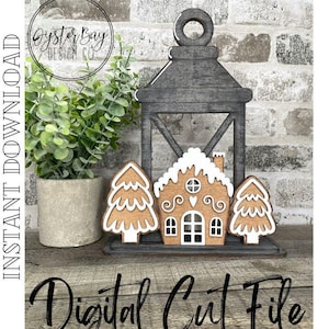 Puede incluir: Un diseño de archivo de corte digital que presenta una casa de jengibre, dos árboles de Navidad y una linterna. El diseño es perfecto para crear una decoración navideña festiva.