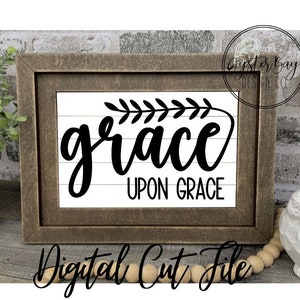 Pu&ograve; includere: Un cartello in legno incorniciato con il testo "grace upon grace" in corsivo nero con un piccolo disegno di ramo con foglie sopra la parola "grace".