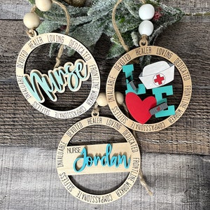 Pu&ograve; includere: Tre ornamenti in legno con la parola "Infermiera" e le parole "Compassionevole, Altruistico, Inestimabile, Devoto, Guaritore, Amorevole, Dedicato, Lavoratore in prima linea" attorno al cerchio. Un ornamento ha un cuore rosso con una benda e una siringa. Un ornamento ha il nome "Jordan".