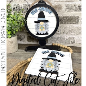 May include: A white wooden sign with a blue and black gnome holding a gold Star of David. The sign says "Sha-Gnome" in blue letters. The gnome is wearing a black hat with a blue band. The sign is on a black stand with a wooden bead garland.