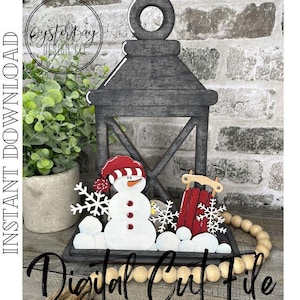 May include: A digital cut file design of a snowman, a sled, and snowflakes inside a black lantern. The lantern has a wooden frame and a black background. The snowman is wearing a red and white hat. The sled is red and has a white base. The snowflakes are white and have a delicate design. The design is perfect for creating a winter-themed craft project.