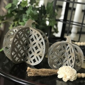May include: Two decorative metal pumpkins with a cut-out design. The pumpkins are painted in a distressed white finish and have a rustic look.