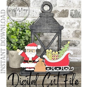May include: A wooden Christmas lantern with a Santa Claus figure, a red sleigh carrying gifts and a Christmas tree. The lantern is gray and has a handle at the top. The words "Digital Cut File" are at the bottom.