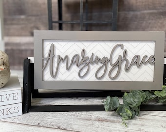 May include: A gray wooden sign with a white chevron pattern background. The sign says "Amazing Grace" in a cursive font.