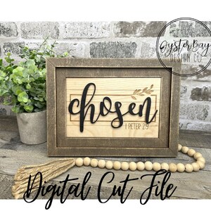May include: A wooden sign with a brown frame and a light wood background. The sign says "chosen" in black script with a small branch of leaves above the word. The scripture reference "1 Peter 2:9" is printed below the word.