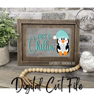 May include: A framed wooden sign with the words "Just Chillin'" in teal script, featuring a cartoon penguin wearing a teal hat. The sign is on a gray wooden background. The words "Digital Cut File" are at the bottom.