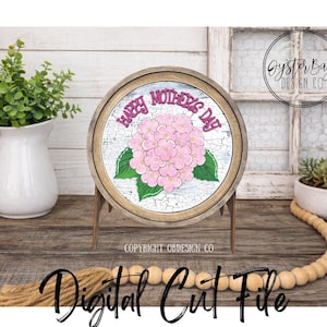 May include: A round wooden sign with a pink hydrangea and the text "Happy Mother's Day." The sign is on a wooden stand. The words "Instant Download" and "Digital Cut File" are also visible.
