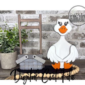 May include: A wooden goose figurine with a white body, orange beak and feet, and decorative eyelashes. A gray picnic basket and a small wooden ladder are also present. The words "Instant Download" and "Digital Cut File" are visible.
