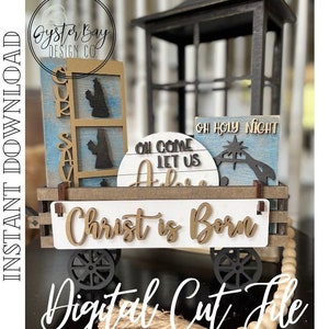 May include: A wooden Christmas-themed wagon with decorative signs. The signs read "Christ is Born", "Oh Come Let Us Adore", and "Oh Holy Night". The wagon has black wheels and a black lantern on top. The words "Instant Download" and "Digital Cut File" are also visible.