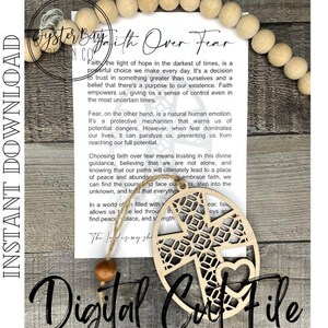 May include: A wooden cutout of a cross with a heart in the center. The cutout is surrounded by a decorative pattern. The cutout is hanging from a string with a wooden bead. The cutout is accompanied by a card with the text "Faith Over Fear" and a message about the importance of faith over fear.