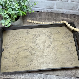 May include: A wooden tray with the words "Dear Santa" and a place for milk, cookies, and carrots. The tray is decorated with snowflakes and a milk bottle.