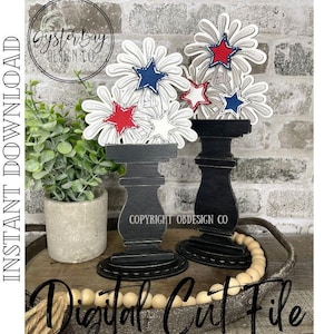 May include: Two black wooden candle holders with white and red firework designs. The candle holders are on a wooden surface with white and brown beads.