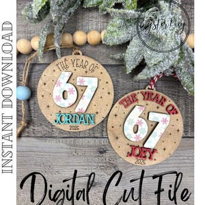 May include: Two round wooden ornaments with the text "The Year of 67" and names. The number 67 is decorated with a floral pattern. One ornament says "Jordan 2026" and the other says "Joey 2025".