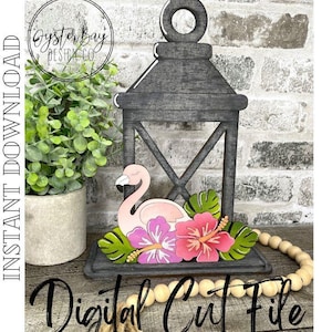Puede incluir: Una linterna de madera gris con un flamenco, flores de hibisco rosas y moradas y hojas verdes. Las palabras "Digital Cut File" están escritas en escritura negra.