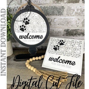 May include: A digital cut file for a welcome sign with a paw print design. The sign says "welcome hope you like dogs".