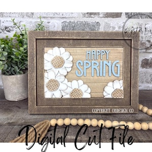 May include: A wooden framed sign with the words "Happy Spring" in light blue letters, surrounded by white daisy flowers. The sign is a digital cut file. The background is a wooden plank design.