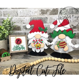May include: Two Christmas gnomes, one in red and white with a candy cane and the other in green and white with a Christmas bauble. A wooden sign with the text "25 Days til Christmas" is in the background.
