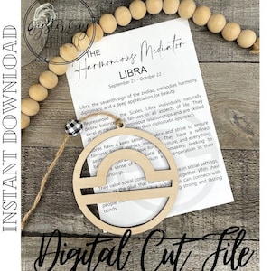 May include: A wooden Libra zodiac sign ornament with a natural finish, hanging by twine. The ornament is in front of a card with text about Libra. The words "Digital Cut File" are at the bottom.