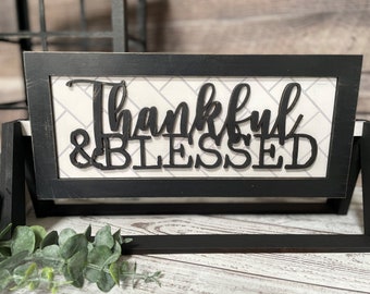 May include: Black framed sign with a white background and a black cutout design that reads "Thankful & Blessed".