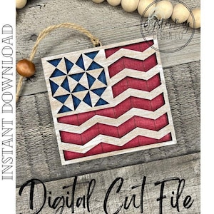 May include: A wooden cutout of an American flag with a geometric star design in the blue field and a chevron pattern in the red stripes. The cutout is hanging from a twine string and is on a woodgrain background.