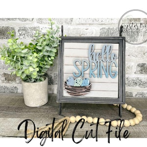 May include: A digital cut file for a wooden sign that says "hello spring" with a nest of blue and green speckled eggs. The sign is on a black stand and there are wooden beads in the foreground.
