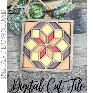 May include: A square, wooden ornament with a geometric design in shades of orange, yellow, and red. The ornament has a starburst pattern in the center and is framed by a light brown border. The text "Digital Cut File" is at the bottom.