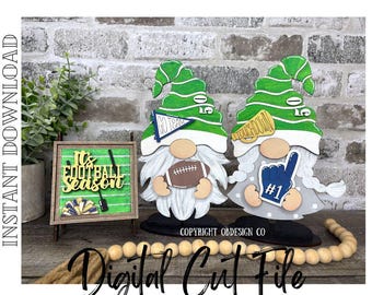 Puede incluir: Dos figuras de gnomos de madera con sombreros verdes y barbas blancas, sosteniendo un balón de fútbol y un dedo de espuma. Un pequeño letrero enmarcado dice "It's Football Season". Los gnomos están sobre una superficie de madera, con una cuerda de cuentas de madera.