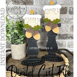 May include: Two wooden candle holders with a white candle and acorn accents. The candle holders are painted black and have a distressed finish. The candle holders are sitting on a wooden tray with a decorative bead garland.