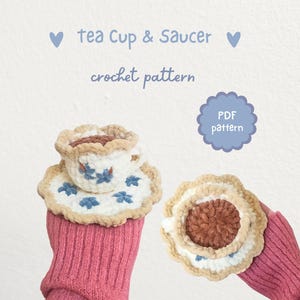 May include: Crocheted tea cup and saucer set with blue floral accents. The set is white with a beige trim. The image includes the text "tea Cup & Saucer crochet pattern" and a "PDF pattern" tag.