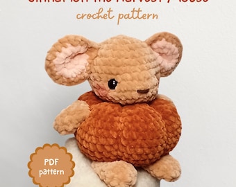 May include: A crocheted mouse toy in shades of brown and orange, with pink inner ears and black eyes. The text "Cinnamon the Harvest Mouse crochet pattern" is displayed above the mouse. A "PDF pattern" badge is also visible.