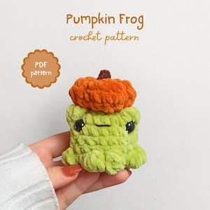 May include: A handmade green crochet frog wearing an orange pumpkin hat. The frog has black eyes and a small mouth. The text "Pumpkin Frog crochet pattern" is visible in the image.