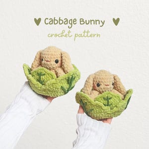 May include: Two beige crochet bunnies nestled inside green crocheted cabbage leaves. The text above reads: ♥ cabbage Bunny ♥ crochet pattern. The bunnies have dark eyes, pink cheeks, and long ears, crafted from soft, textured yarn material.