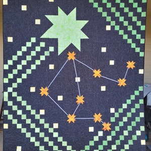 May include: A black quilt with a green and white checkered pattern and a constellation of orange stars on a dark blue background. A large green star is in the upper center of the quilt.