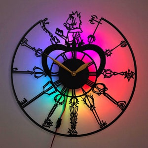 May include: A black metal clock with a rainbow background and a silhouette of a character holding a key. The clock has a black face with gold hands and Roman numerals.