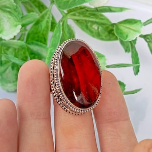 May include: A silver ring with a large, oval-shaped, red gemstone set in a decorative bezel.