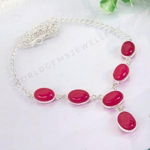 Può includere: Una collana a catena d'argento con sei pietre preziose rosa di forma ovale. La collana ha un ciondolo con una singola pietra preziosa rosa.