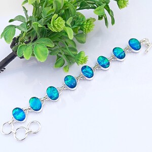 May include: A silver bracelet with oval-shaped blue opal gemstones. The bracelet has a lobster clasp closure and is made of sterling silver.